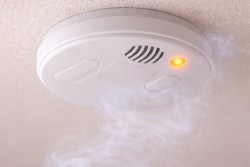 "Close-up van een witte rookmelder aan een plafond met lichte rook