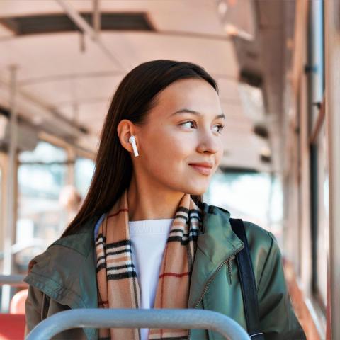 Vrouw luistert lachend naar podcast in de bus 