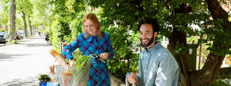 man zit op muurtje en vrouw haalt boodschappen uit fietsmand